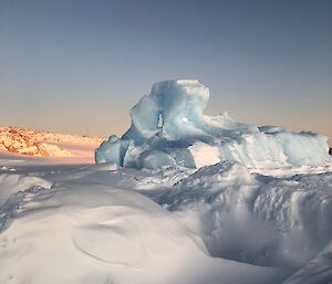 Iceberg on sea ice surrounded by snow with rocks in the background