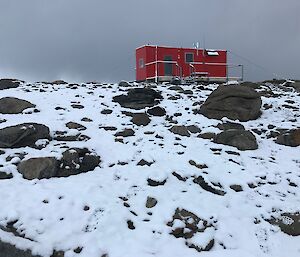 Robbo’s hut on a snow and rock covered hill with storm clouds in the background