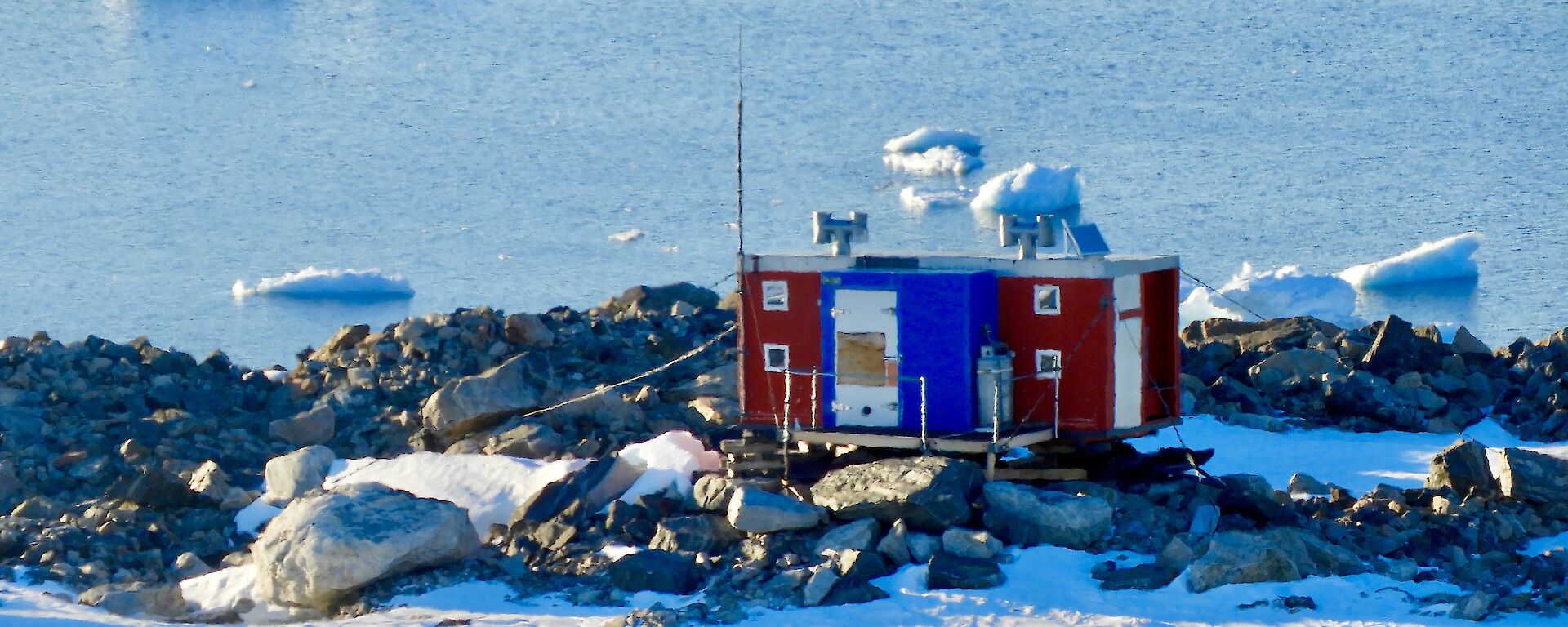 Jack’s Donga which is red and blue sitting on rocks overlooking icebergs and the water