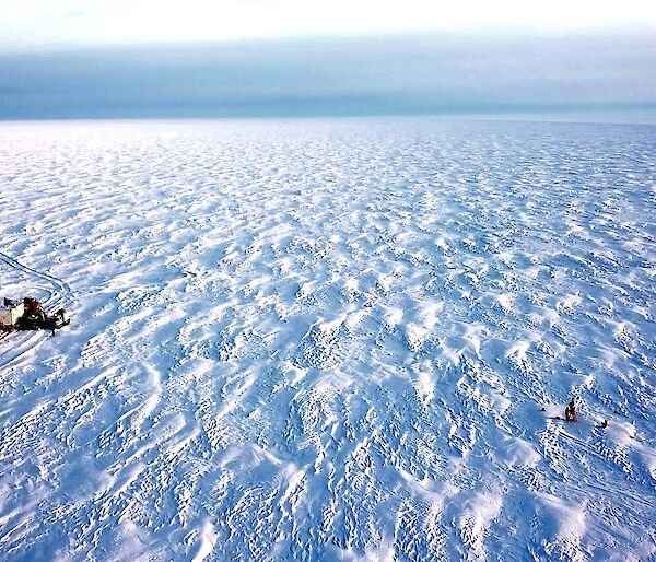 A drone shot of the traverse group of vehicles and the Automsted Weather System being worked on surrounded by snow and a grey sky