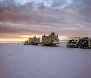 A tractor and vans followed by a green Hagglund making its way down towards Casey and a setting sun