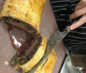 Cutting a pastry to serve the Beef Wellington on a cutting board