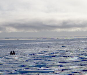 Two quads in the distance on the sea ice under a partly cloudy sky
