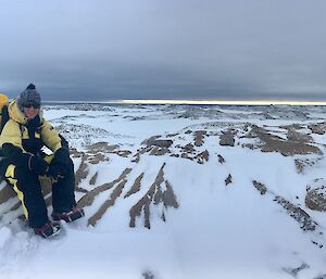 CHris sitting on a rock on the top of a hill on a cloudy day