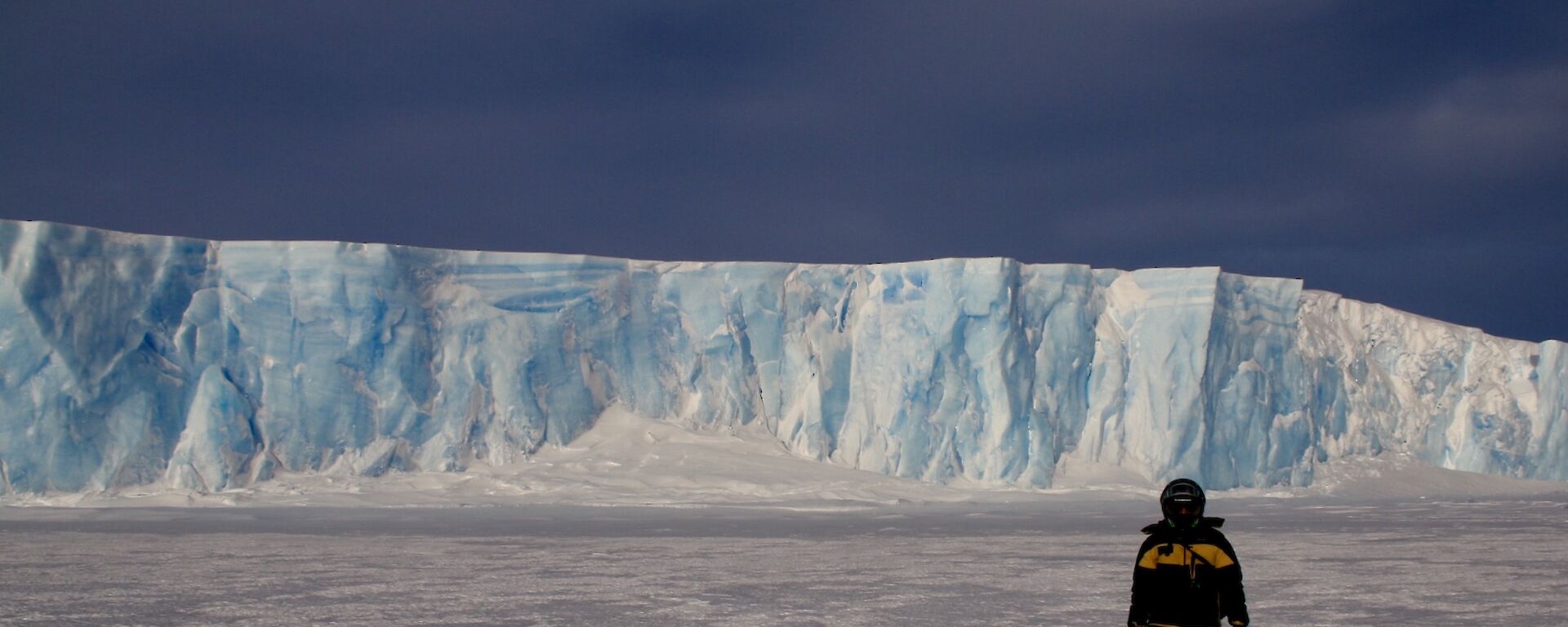 Jordan standing on the sea ice in froont of the sea ice cliffs of light blue and white