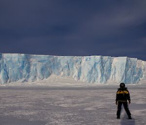 Jordan standing on the sea ice in froont of the sea ice cliffs of light blue and white