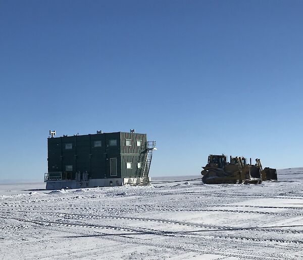 A dozer towing the green Wilkins mess building into the summer location