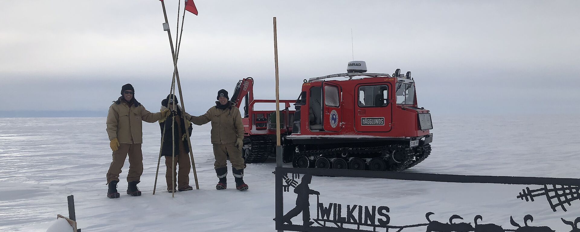 Three cane team members, holding the canes, with the red hagg and the wilkins sign in view on a cloudy day