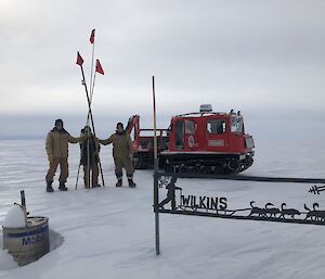 Three cane team members, holding the canes, with the red hagg and the wilkins sign in view on a cloudy day