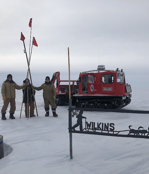 Three cane team members, holding the canes, with the red hagg and the wilkins sign in view on a cloudy day