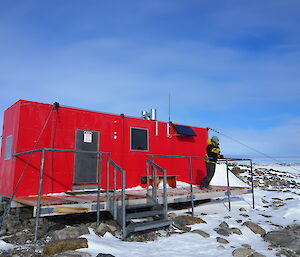 Jordan standing on the deck of Robbo’s hut on a clear, sunny day