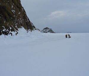 Three expeditioners walking on sea ice along the rugged coast line of Peterson Island
