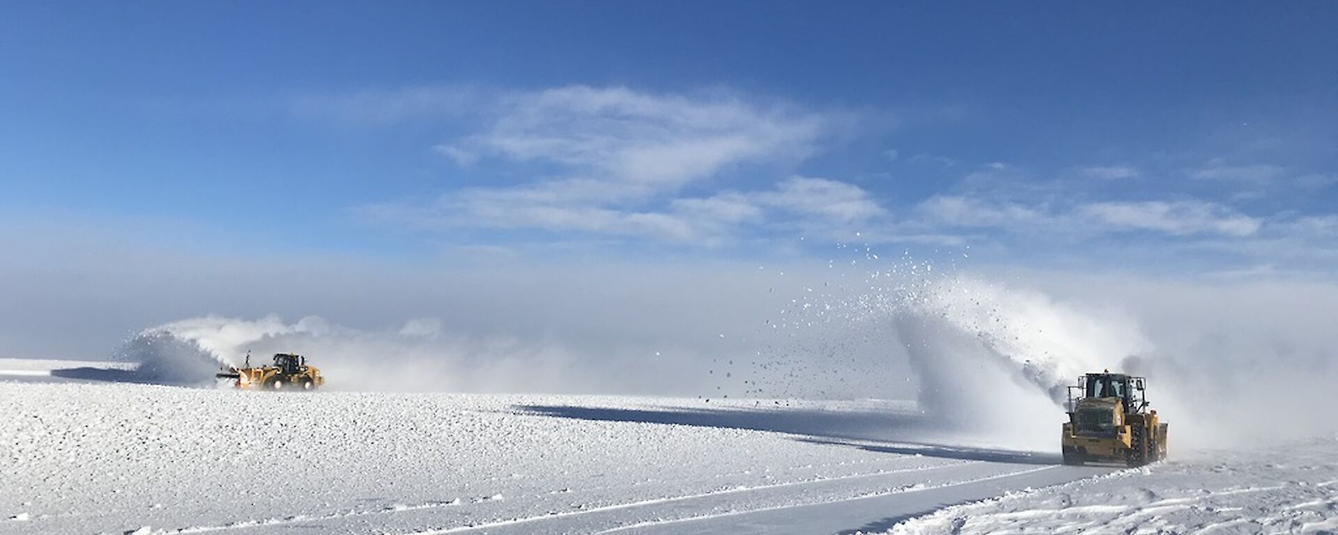 Two snow blowers blowing snow on a clear day