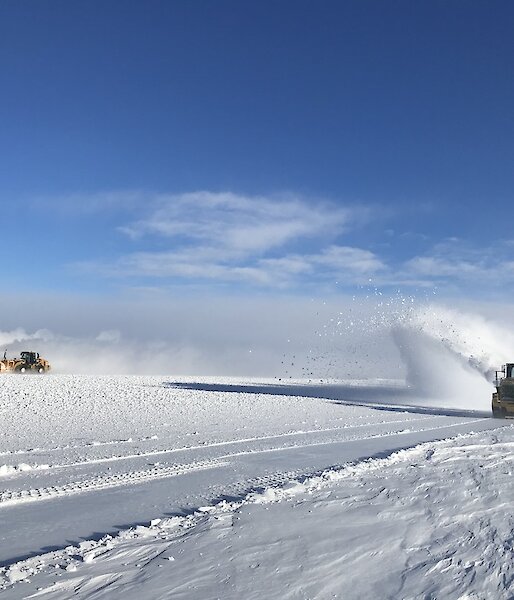 Two snow blowers blowing snow on a clear day