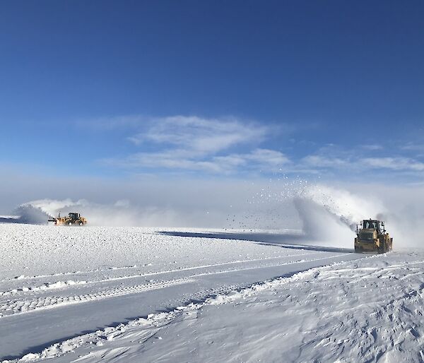 Two snow blowers blowing snow on a clear day