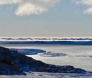 a horizon of icebergs with a rocky slope and ice in the foreground