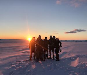 Sun setting behind group of expeditioners standing on the snow