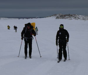 Seven expeditioners skiing to wilkes with vehicles and water in the distant background