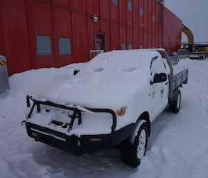 A blanket of snow covers a ute outside the red shed at Casey