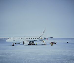 An A319 is parked on the runway, with passengers disembarking