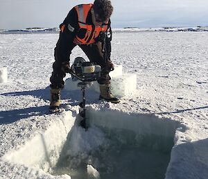 Ben Keyes drilling the corners of the tide gauge pool cut in the sea ice to let in the sea water — and the tide