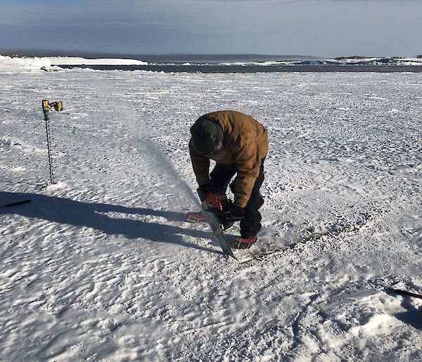 Nathan E using a chainsaw in the sea ice to define a pool for the tide gauge