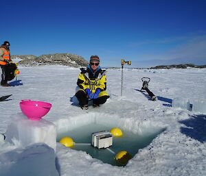 A lady dressed in yellow overlooking a water filled square cut into the sea ice.