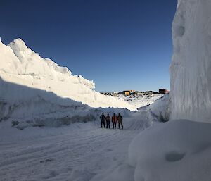 Four men on a snowy road with tall stacks of snow on either side of them.