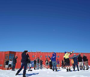 Expeditioners outside Casey’s Red Shed looking up at a Qantas plane in the sky