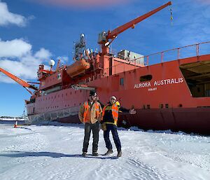 Two men standing in front of a big orange ship