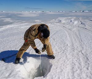 Engineer Mike crouches over a drill hole while checking its depth with a measuring tape.