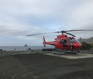 Helicopter on the helipad on the isthmus, Macquarie Island with the AA in the background in Buckles Bay