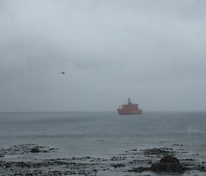 The Aurora Australis at anchor in Buckles Bay and the first helicopter coming ashore for resupply at Macquarie Island