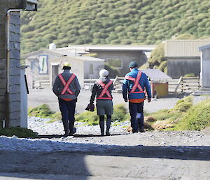 Three expeditioners walking around station during resupply with high visibility vests on