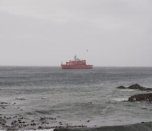 A helicopter brings in a sling load to station with the Aurora Australis in the background