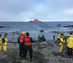 8 people stand on a beach waiting for a small boat