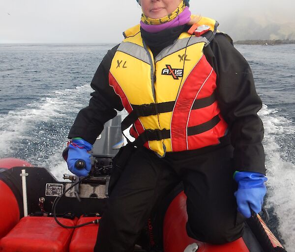 a woman in a life jacket sits at the tiller of a red inflatable boat