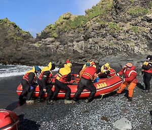 a team of 10 people land a boat on a rocky beach