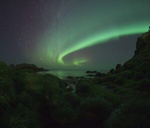 a bright green aurora swirls over a cove of water at night