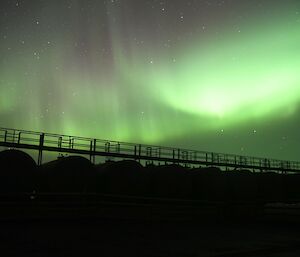 a bright green flash of light hangs over a row of black fuel tanks