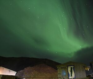 a shadow of green light hangs over some wooden buildings lighting up the night sky