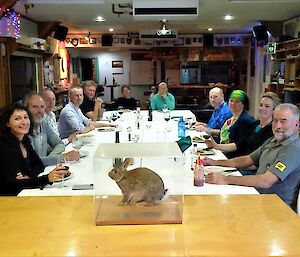 A group of people sit around a large table with a rabbit in a glass cabinet in front of them