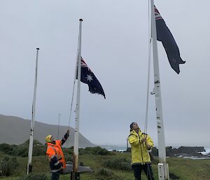 Two people lower the Australian and New Zealand flags