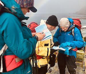 Three people in hiking gear are looking at maps