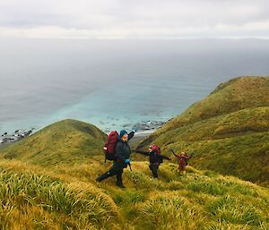 three people hike along a green tussock covered ridge
