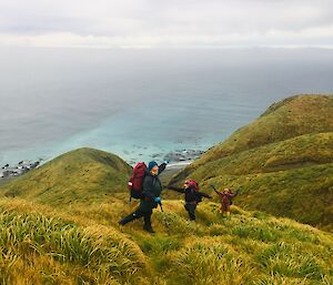 three people hike along a green tussock covered ridge