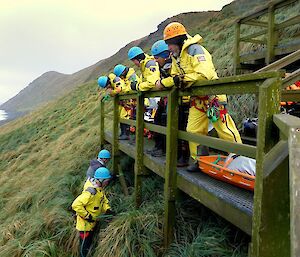 Five people are looking over the edge of a platform as two people tie knots to a structure