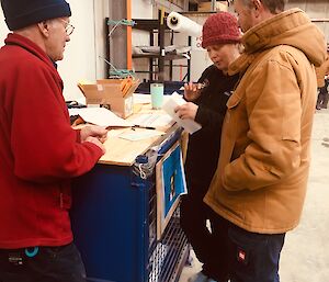 Three people stand around a cage pallet holding paperwork