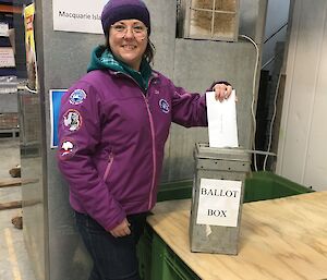 A woman in a purple jacket puts a ballot paper in the ballot box