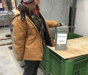 a woman in a beanie puts a ballot paper into a ballot box